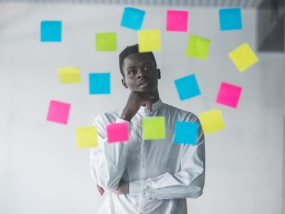 Young afro american business man standing in front of stickers glass wall and looking on futures plans at his office place